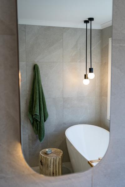 Mirror view of a modern bathroom with freestanding bath, grey tiles and pendant light