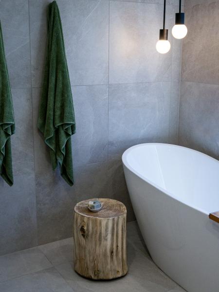 Modern bathroom corner with freestanding bath, grey wall tiles, timber stool and hanging towels