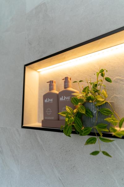 Illuminated recessed shower niche with bathroom products and trailing greenery