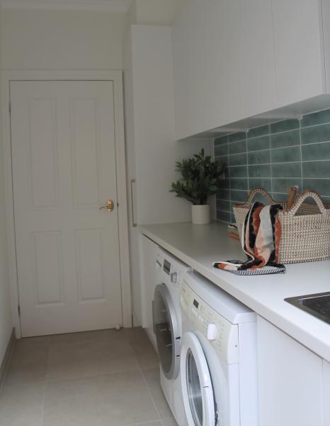Bright laundry renovation with white cabinetry, front-load washers and green tiled splashback