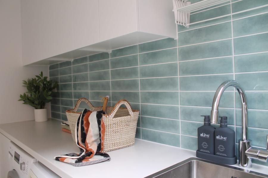Laundry bench with woven basket, plant and glossy aqua subway tile splashback