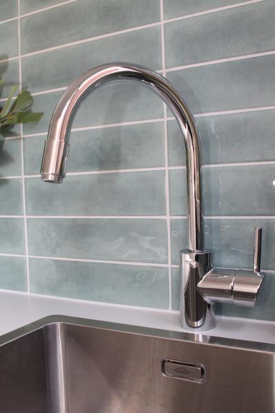 Chrome kitchen tap above a stainless steel sink with soft green subway tiles