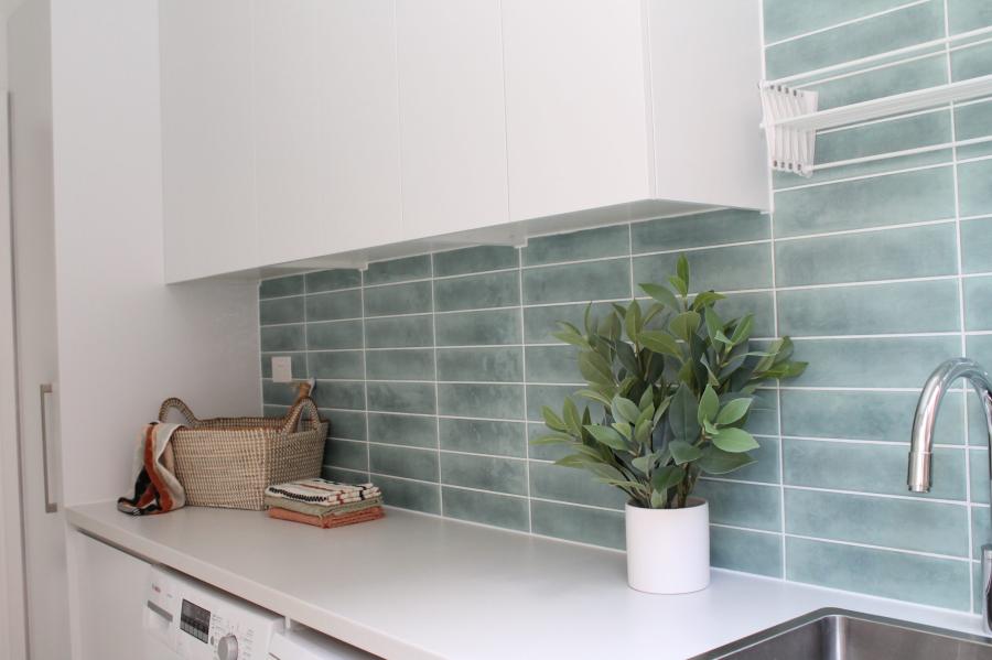 Modern laundry with green subway tile splashback, white cabinetry and benchtop