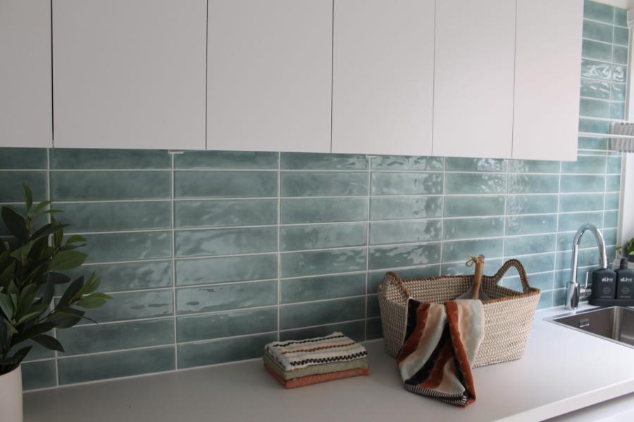 White overhead cabinets above a green tiled splashback and benchtop in a modern laundry