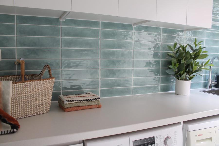 Laundry bench with glossy green subway tile splashback, white cabinetry and potted plant
