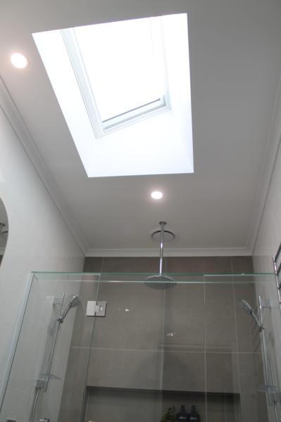 Modern bathroom with skylight above a frameless glass shower and recessed ceiling lights