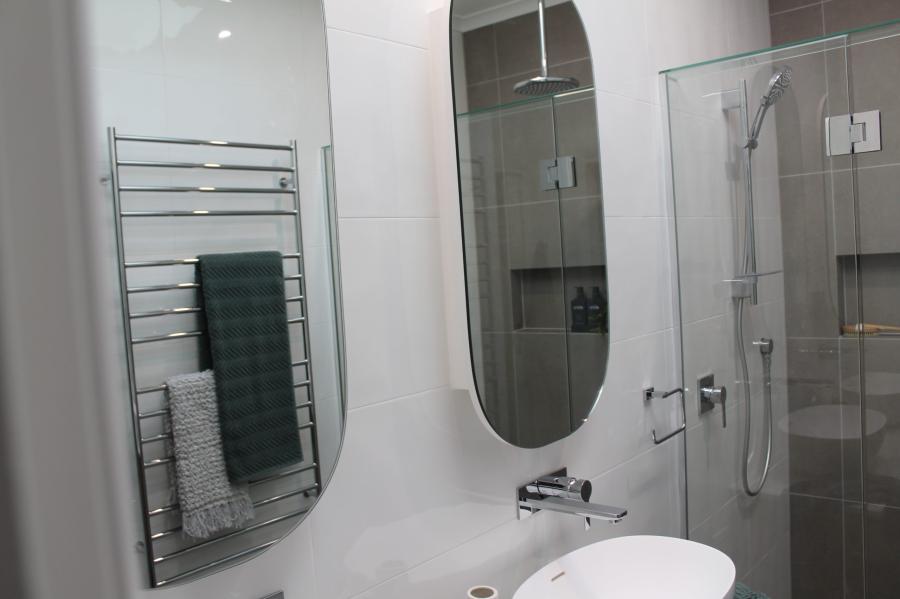 Modern bathroom with oval mirror, wall-hung basin, glass shower and heated towel rail