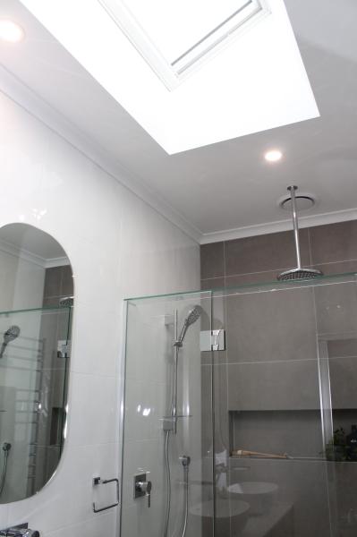 Modern bathroom with skylight, arched mirror and frameless glass shower