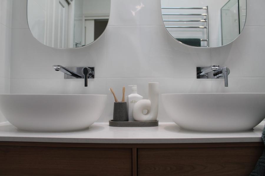 Double vessel basins on timber vanity with round mirrors in a modern white bathroom