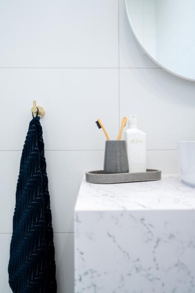 Marble-look bathroom vanity with soap dispenser, toothbrush holder and dark towel on tiled wall