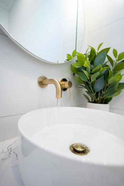 White vessel basin with brushed brass tapware beneath a round mirror