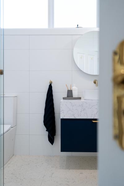 Modern white tiled bathroom with floating vanity, round mirror and brass tapware