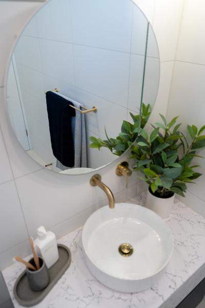 Round mirror above vessel basin with brushed brass tapware in a white tiled bathroom