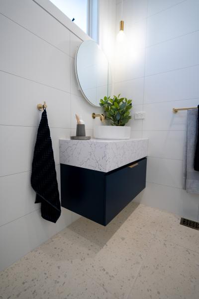 Compact modern bathroom vanity with round mirror, brass tapware and white tiled walls