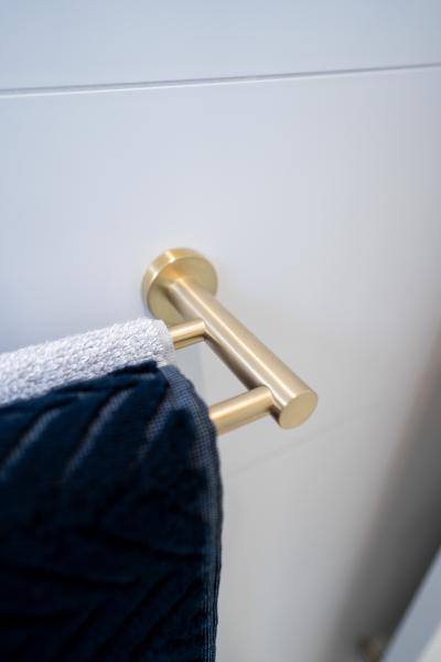 Brushed brass towel rail on a white tiled bathroom wall with folded towels