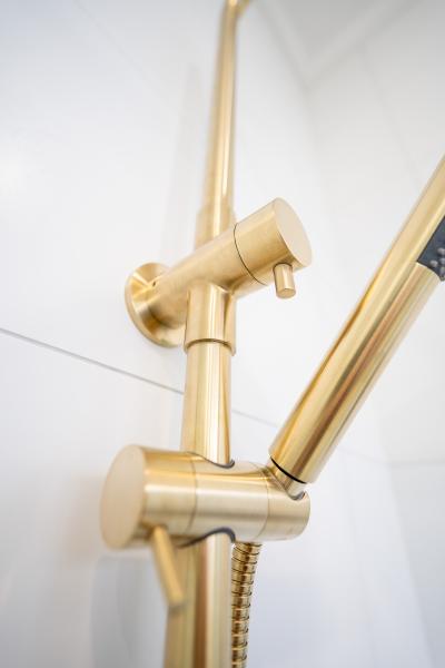 Brushed brass handheld shower rail and mixer detail on a white tiled bathroom wall