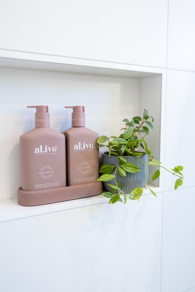 Two mauve pump bottles and a trailing plant on a recessed white bathroom shelf