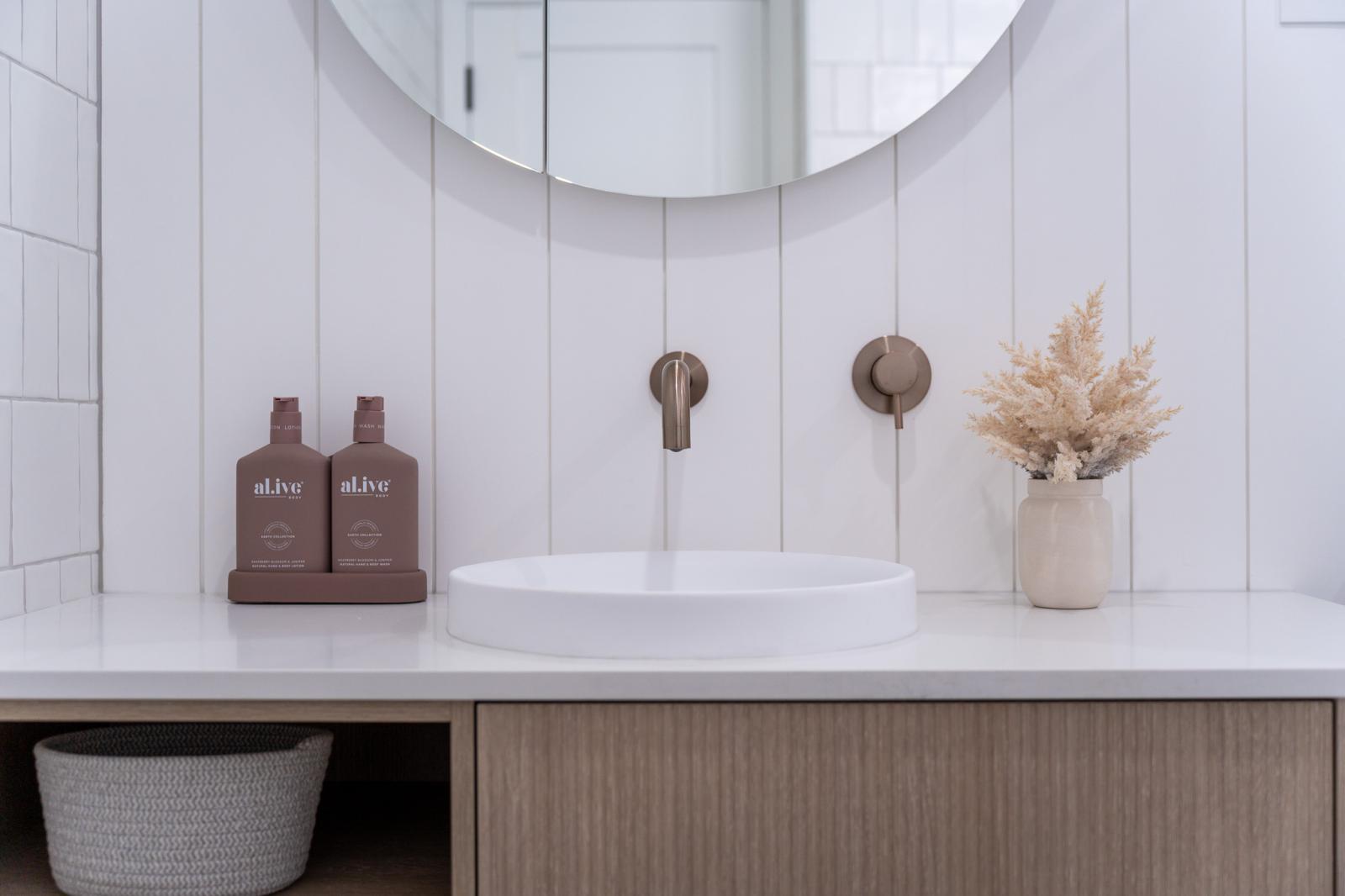 Modern bathroom vanity with vessel basin, round mirror and brushed brass wall taps
