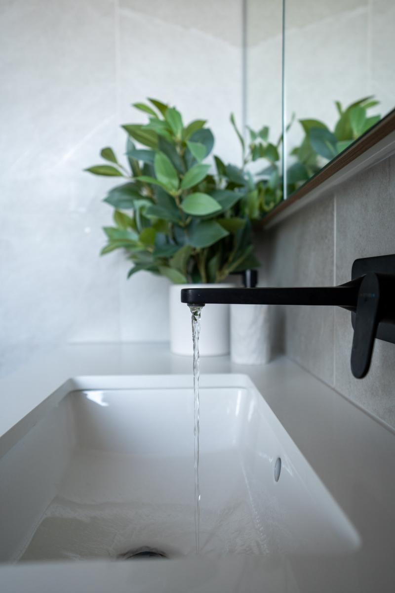Black wall-mounted tap with water flowing into white basin