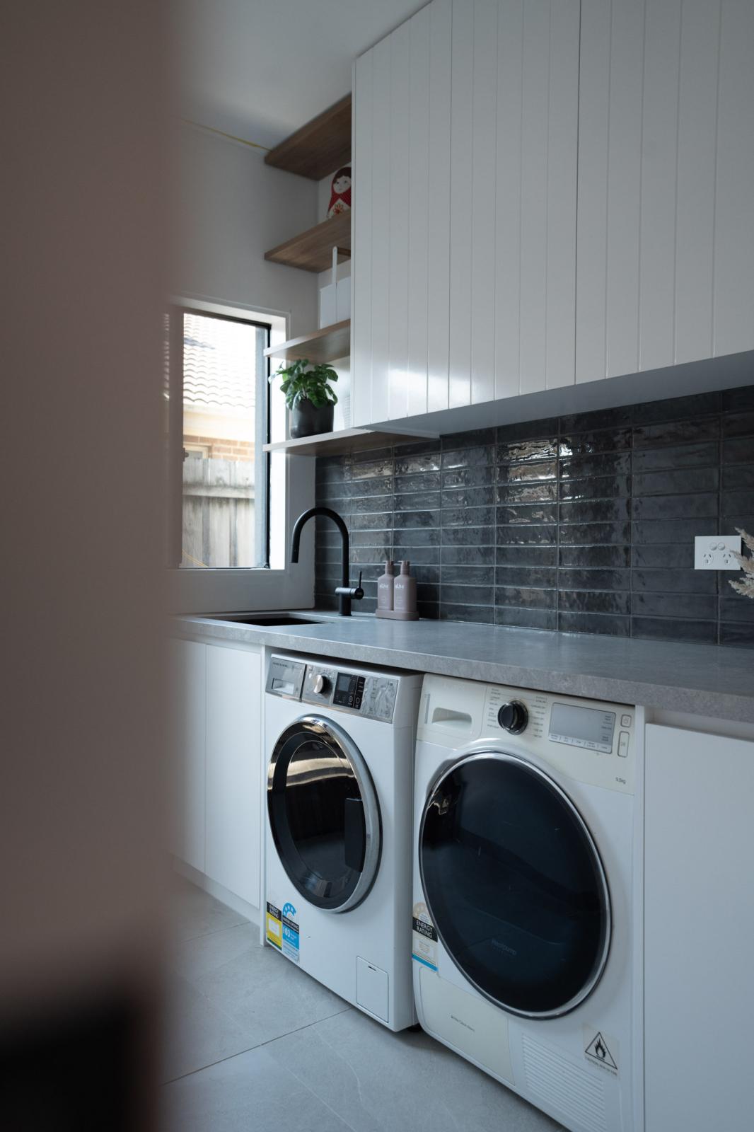 Modern laundry room with washing machines and dark tile splashback
