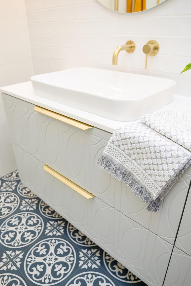 White vessel basin on vanity with brass tapware and patterned bathroom floor tiles