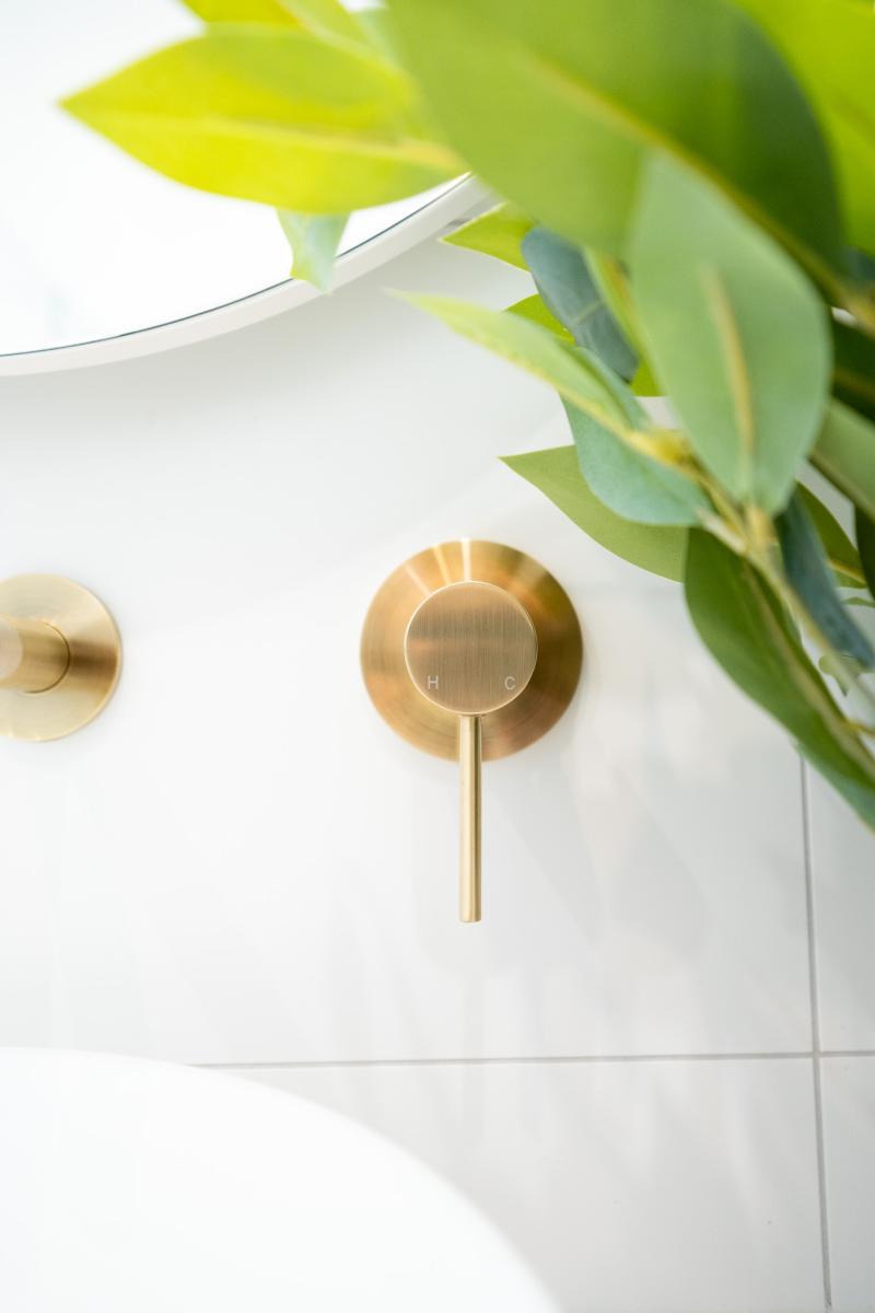 Brass wall-mounted mixer tap with white tiles and greenery