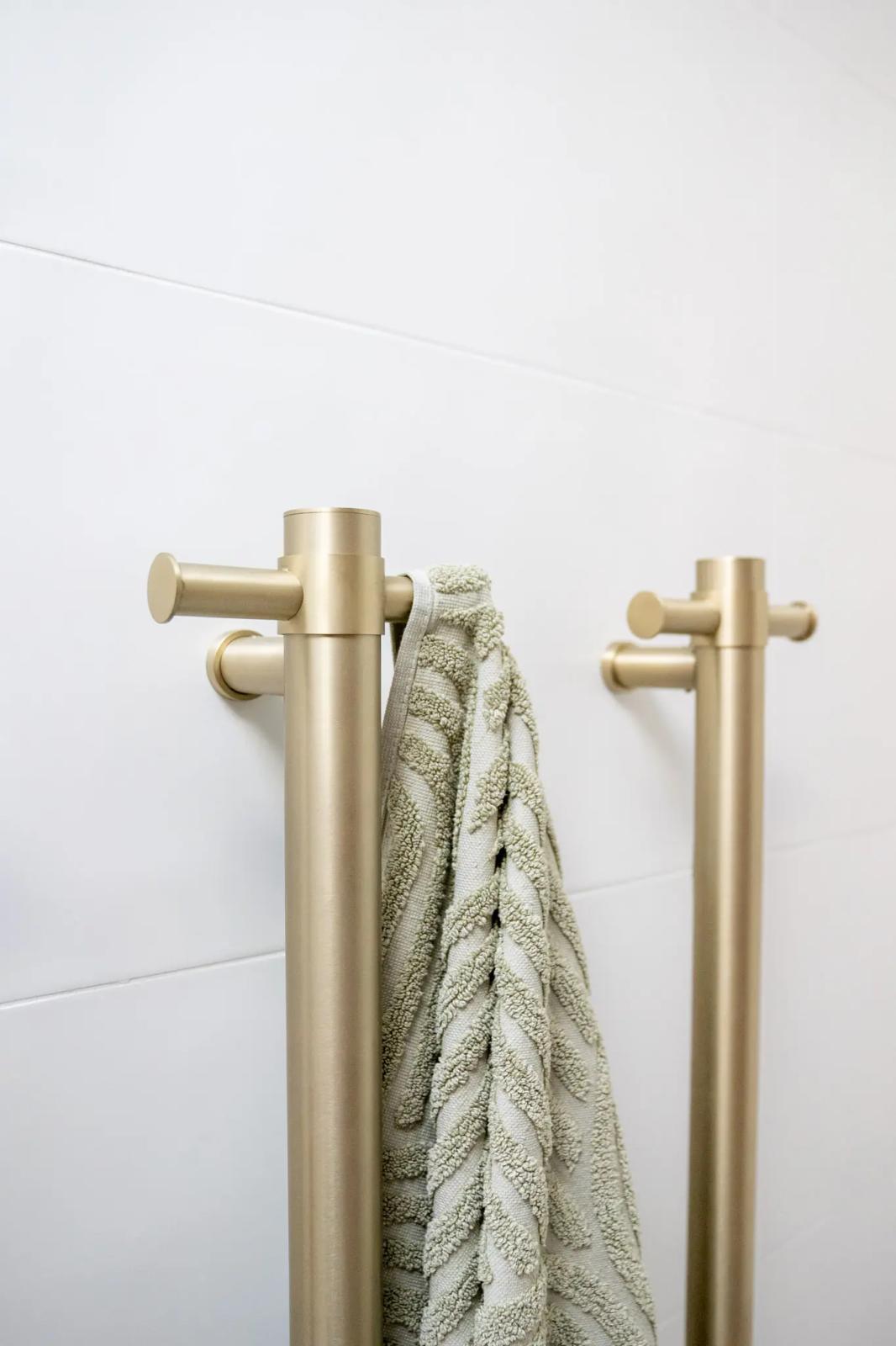 Brushed brass towel rail and robe hook on a white tiled bathroom wall
