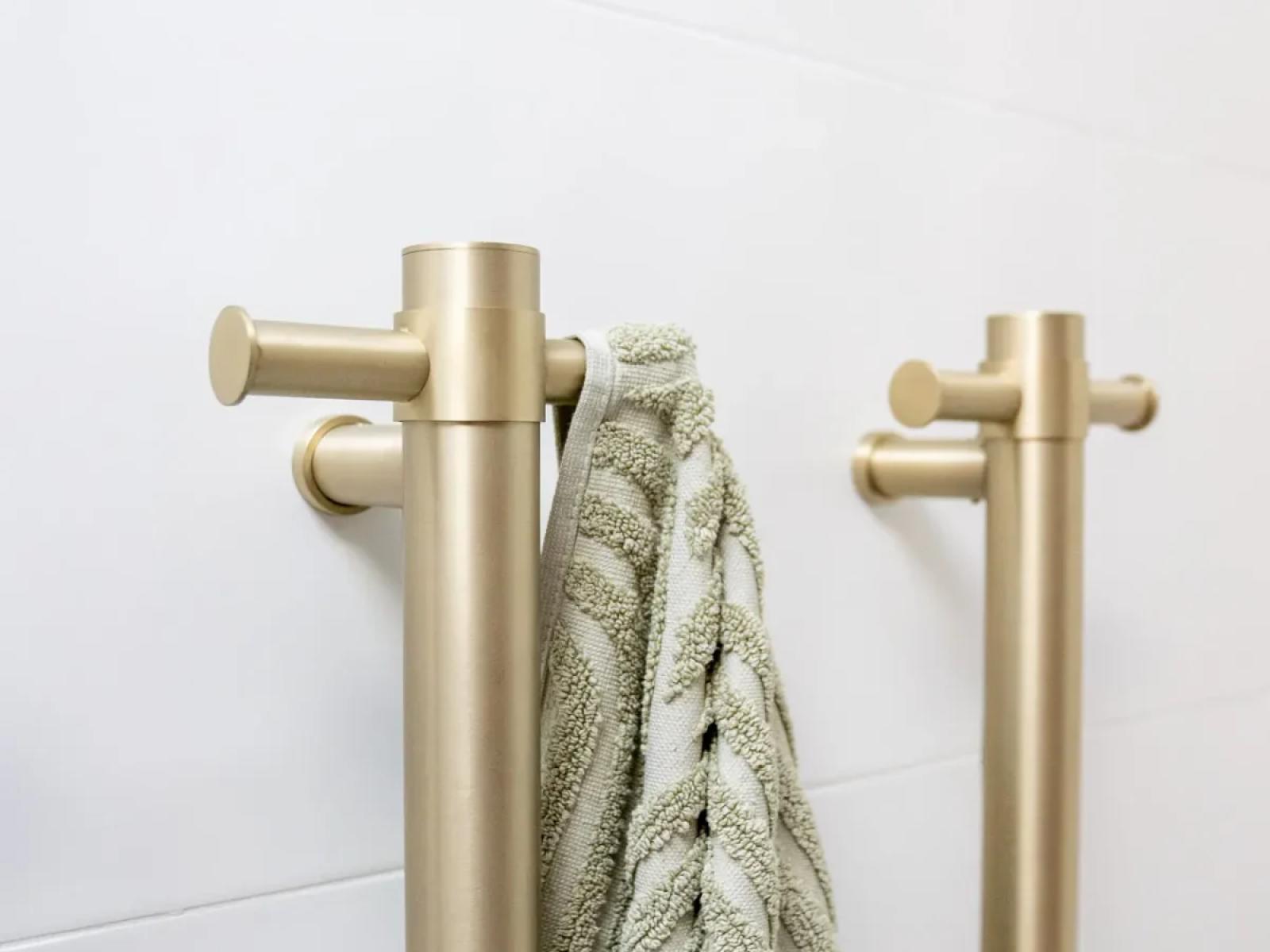 Brushed brass towel rail with hanging towel against white tiled bathroom wall