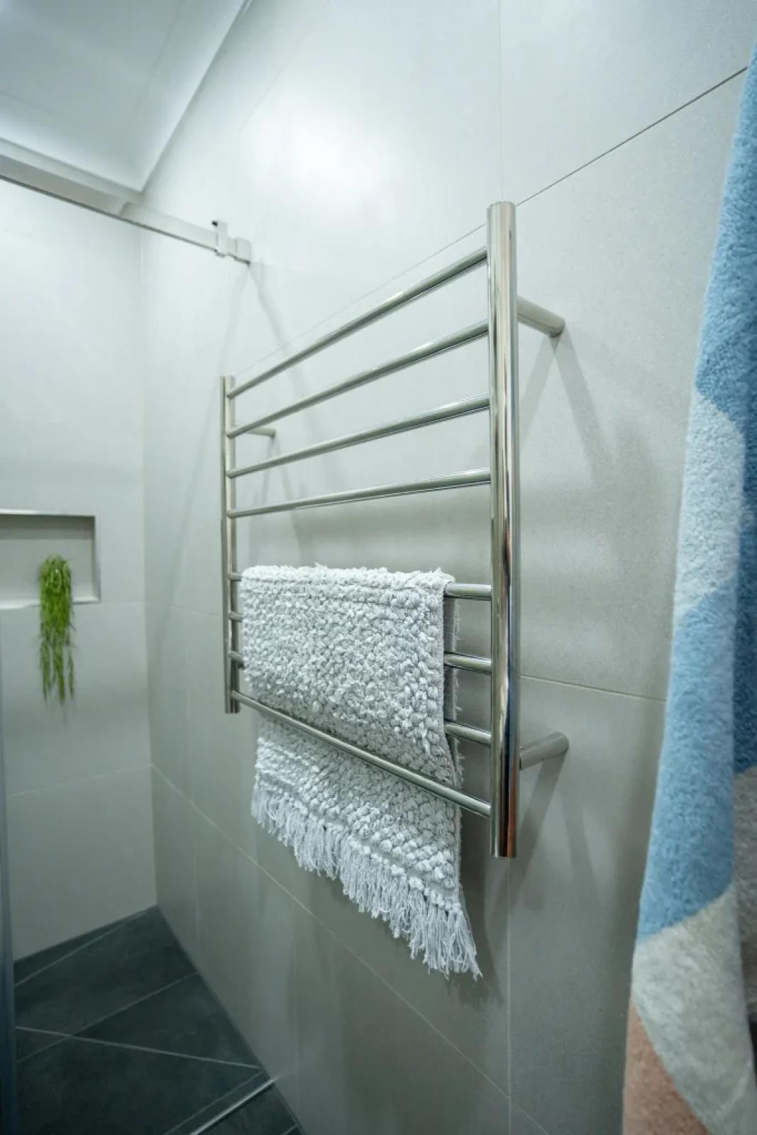 Chrome heated towel rail with folded white towels on a tiled bathroom wall
