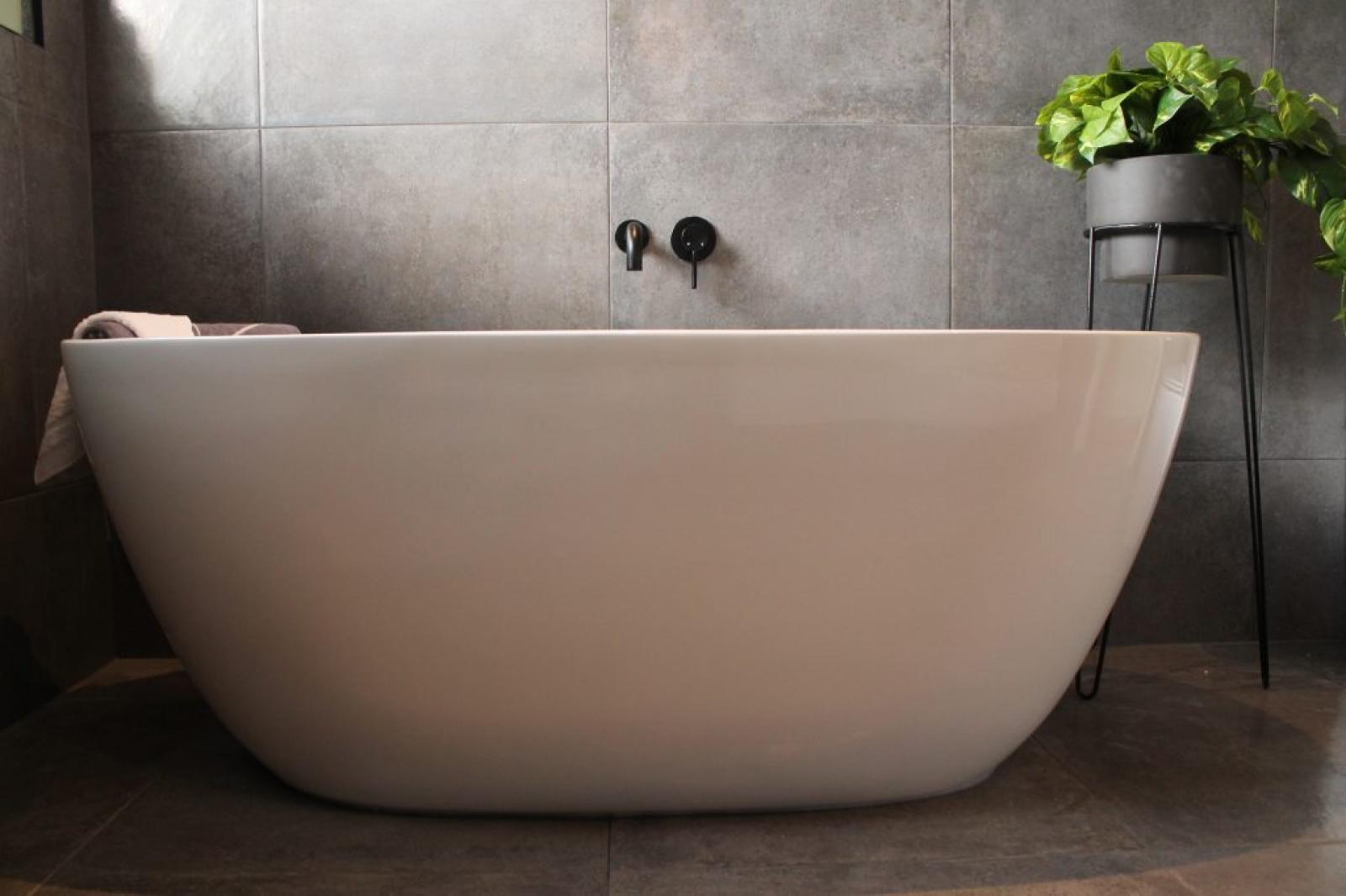 Freestanding white bath against grey tiled bathroom wall with potted plant