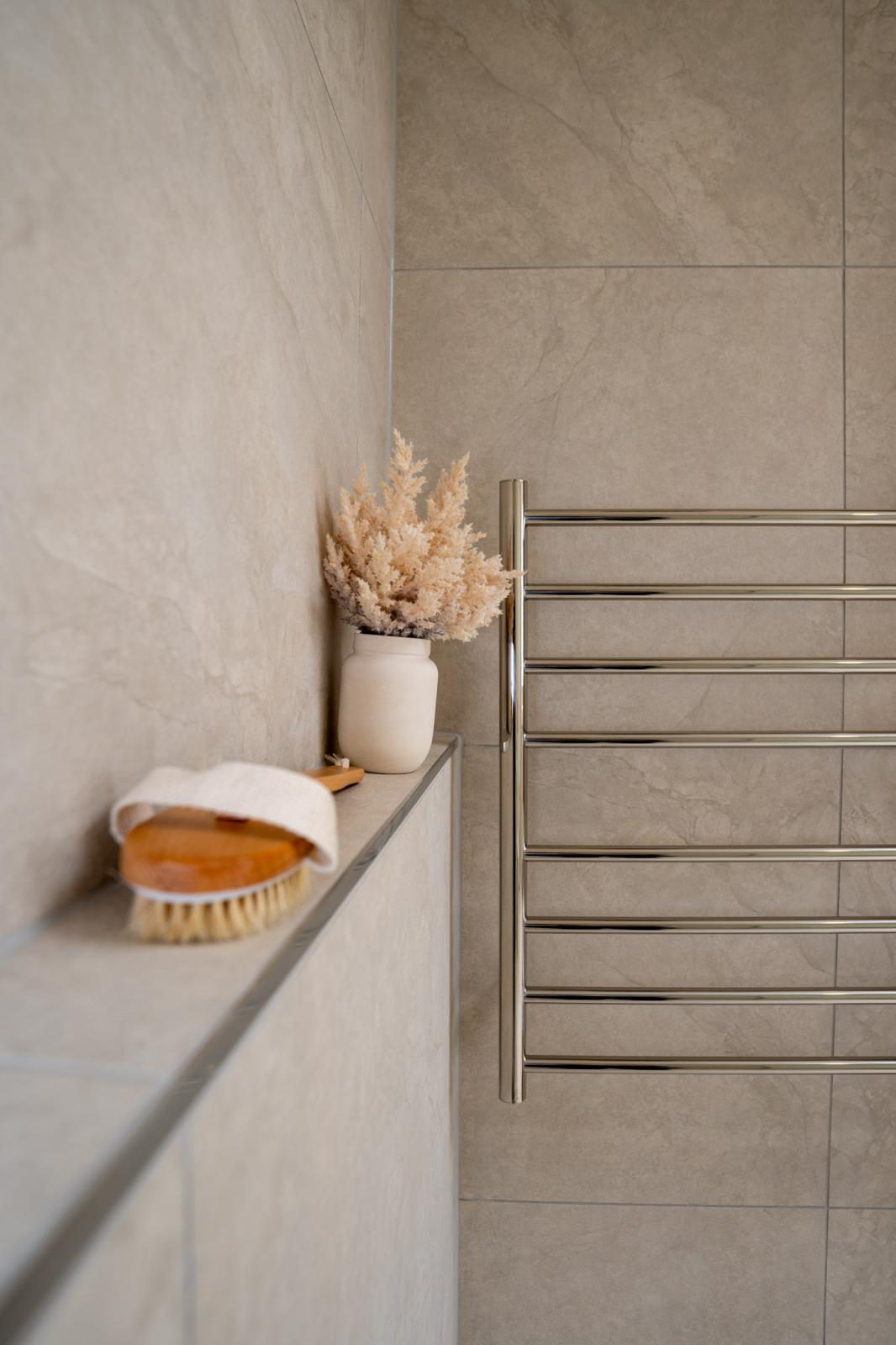 Modern bathroom shelf with white ceramic holder, dried pampas grass, and wooden brush beside towel rail