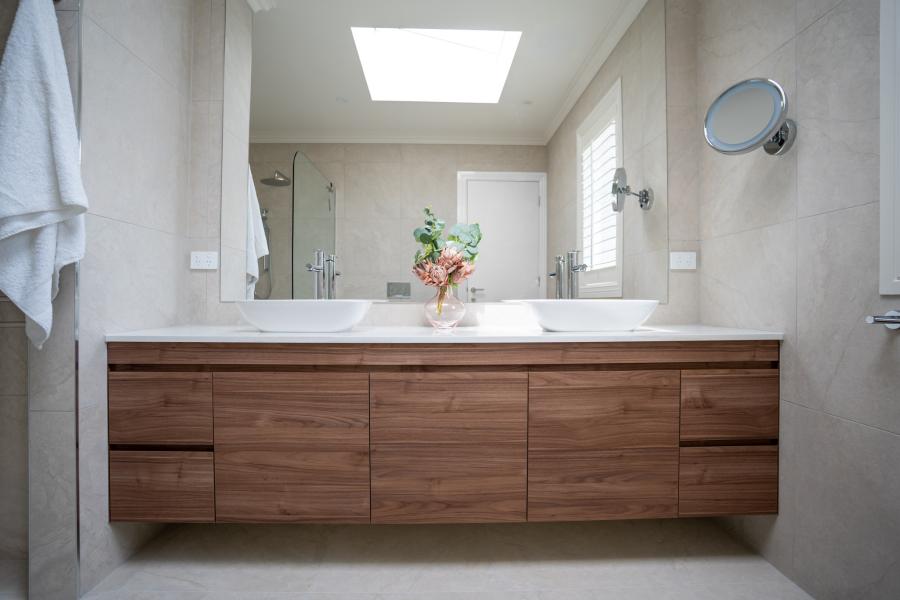 Modern bathroom vanity with timber cabinetry, dual white basins, and large illuminated mirror