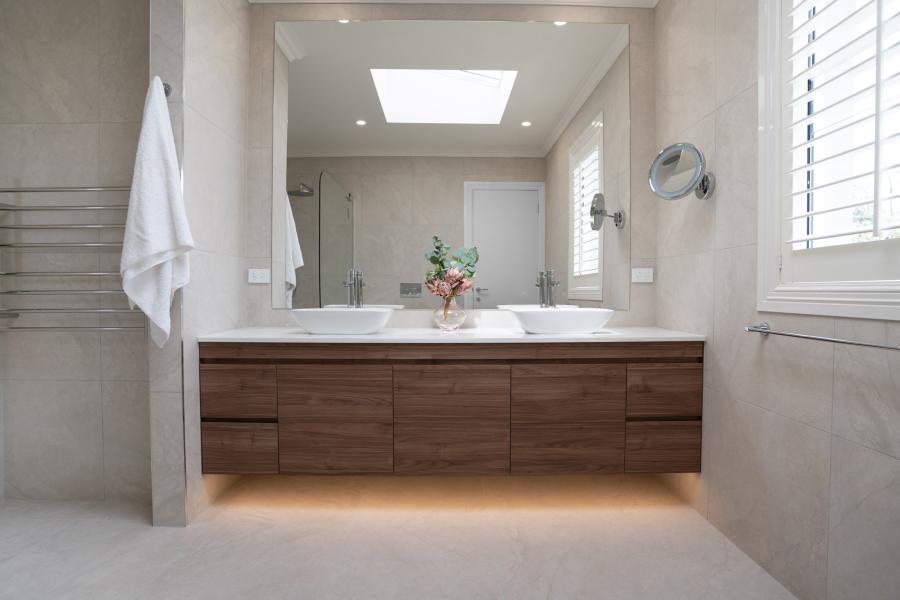 Modern bathroom with timber vanity, large mirror, and under-bench lighting