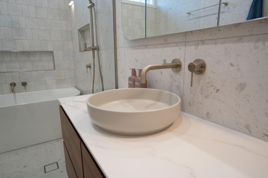 Modern bathroom vanity with vessel basin, wall-mounted tapware and white tiled shower area