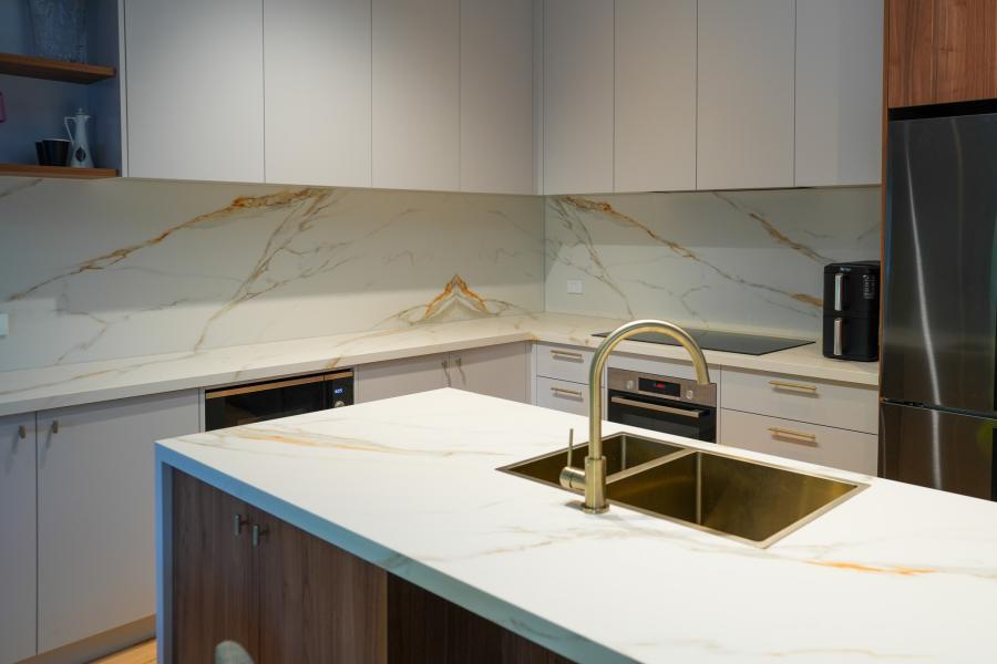 Modern kitchen with white stone island, brass tapware, integrated sink and timber cabinetry