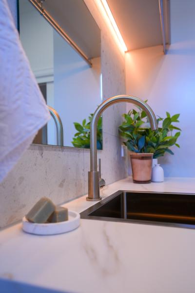 Brushed metal bathroom tap beside a stone basin with mirror and potted plant