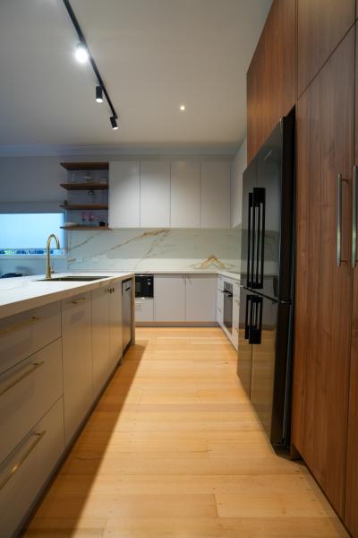 Modern galley kitchen with timber cabinetry, white benchtops and black built-in appliances