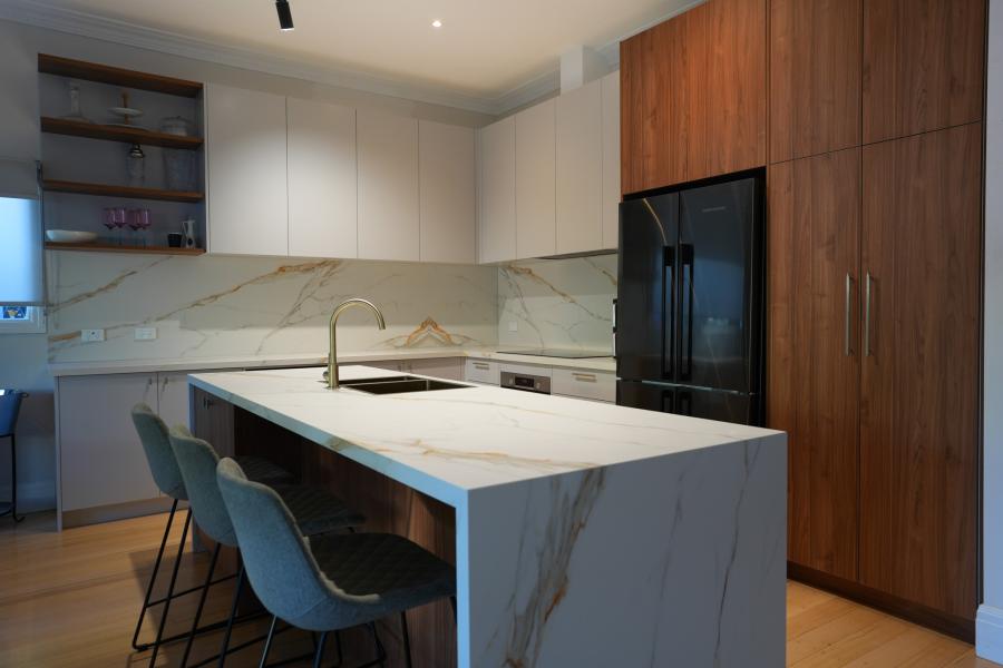 Modern kitchen with marble-look island, black fridge, timber cabinetry and pendant-style seating