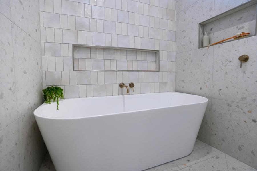 Freestanding white bath beneath tiled wall niches in a modern bathroom