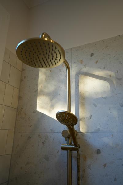 Brushed brass rainfall shower with handheld shower on light stone-look bathroom tiles
