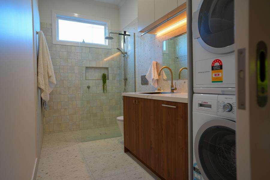 Combined bathroom and laundry with walk-in shower, timber vanity and stacked washer dryer