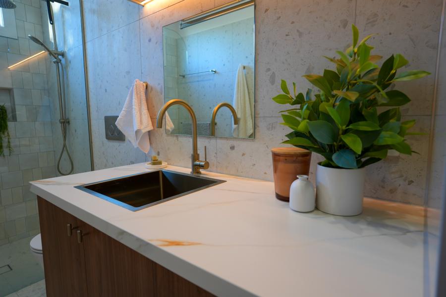 Modern bathroom vanity with vessel basin, brushed brass tapware and mirror beside a glass shower