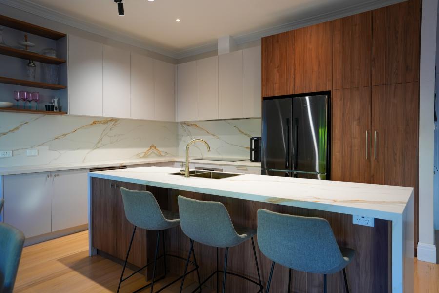 Modern kitchen with white island, timber cabinetry and four bar stools